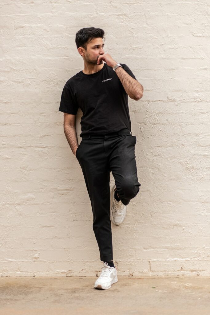 man in black crew neck t-shirt and blue denim jeans leaning on white wall